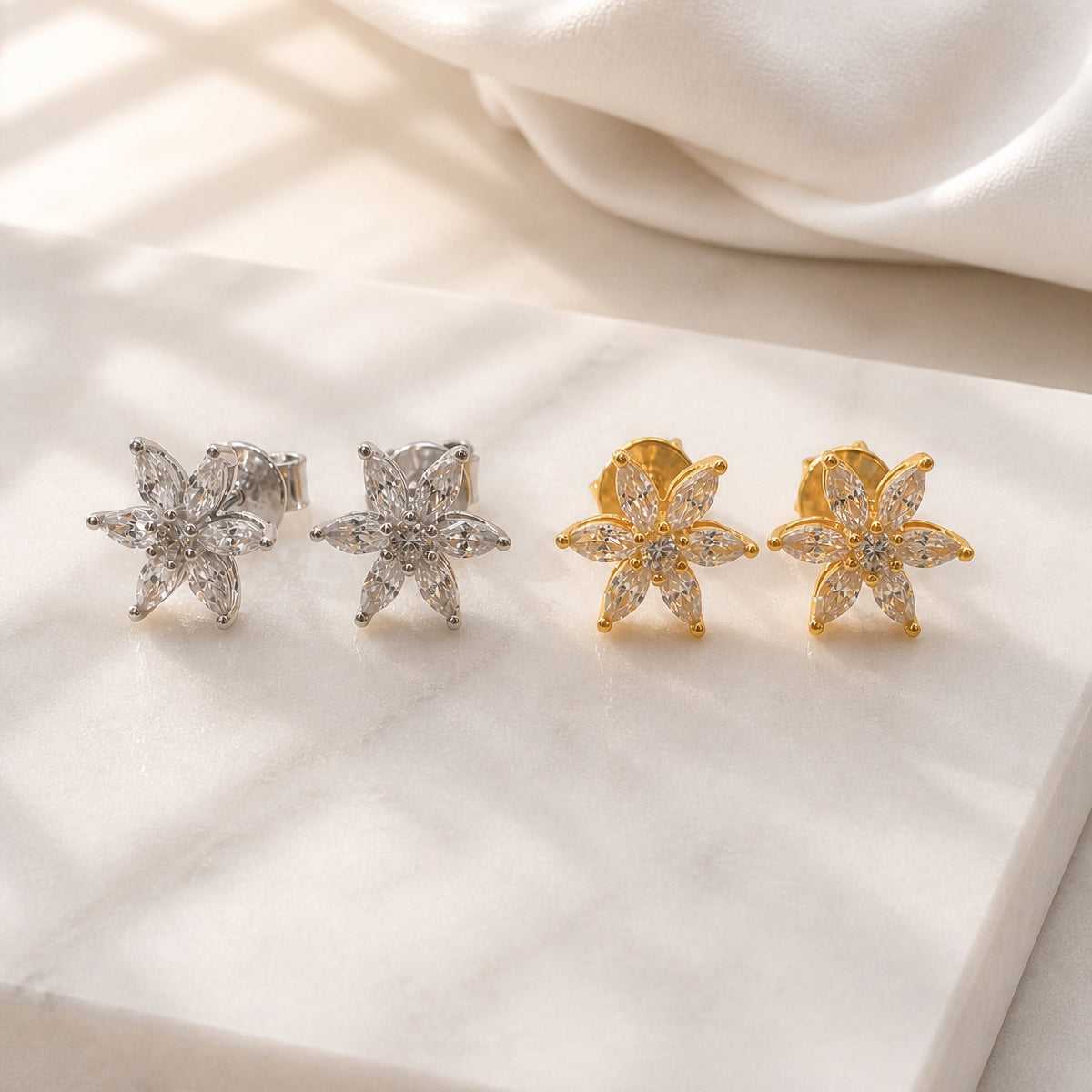 Pair of silver and gold flower-shaped earrings on a soft fabric background
