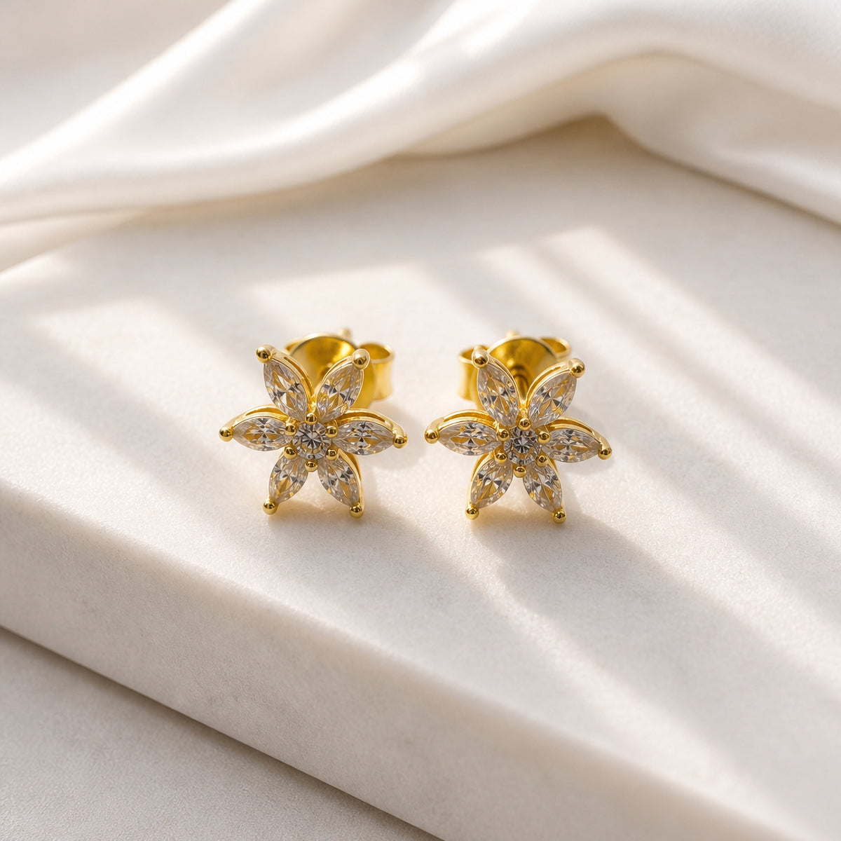 Gold flower-shaped earrings with clear stones on a white fabric background